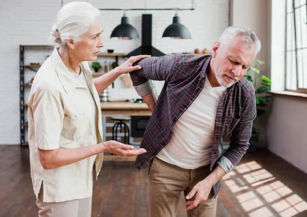Older man with support from his wife because he has a very sore back. His wife looks concerned for him and will suggest a course of pain management
